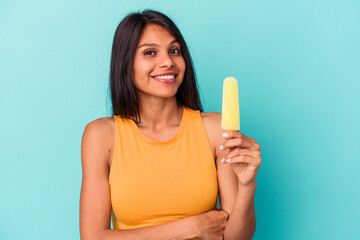 Young latin woman holding ice cream isolated on blue background laughing and having fun.