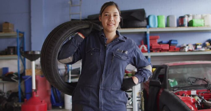 Portrait of female mechanic holding a tire and smiling at a car service station