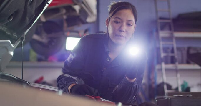 Female mechanic using a torch light and repairing a car at a car service station