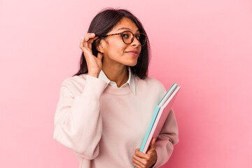 Young student latin woman isolated on pink background trying to listening a gossip.