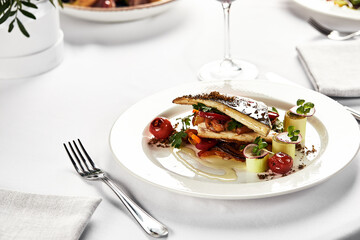 Grilled sea bass with fried tomatoes, close-up of grilled fish on a light plate, grilled sea bass with a glass of wine, holiday table.