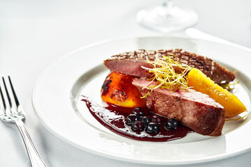 Grilled duck breast with peaches in berry sauce, grilled duck fillet on a white plate, close-up of...
