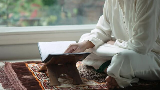 Asian Muslim middle-aged man sitting and reading the Qur'an at his home during the month of Ramadan, 4k resolution.
