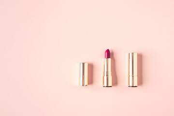 Decorative cosmetics composition of mockup lipsticks in golden casings on pastel pink background. Cosmetics concept. Flat lay style. Copy space.