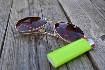 Cool pilot sun glasses isolated on a wooden table with a green lighter for smoking