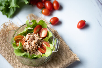 Tuna salad with fresh oak greens and tomatoes in a cup on wooden background
