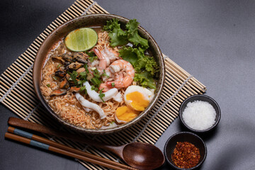 Instant noodles with seafood tom yum, prawns, squid, mussels in a brown ceramic bowl