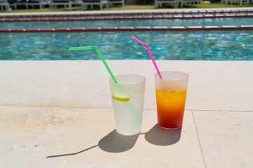 Summer fruit alcoholic cocktails with colored straws stand by the pool.