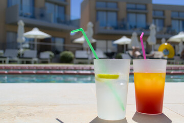 Fruit alcoholic cocktails with multicolored tubes stand against the backdrop of the pool.
