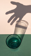 Green drinking glass with harsh glass and human hand shadows on colored background.