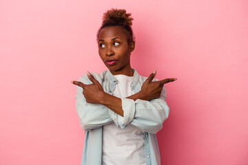Young african american woman isolated on pink background points sideways, is trying to choose between two options.