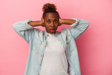 Young african american woman isolated on pink background covering ears with hands trying not to hear too loud sound.