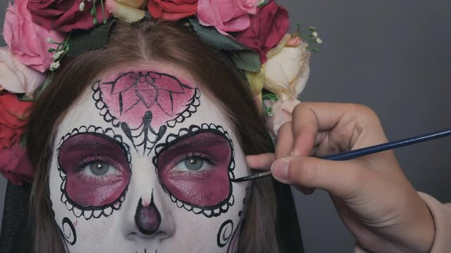 Halloween makeup for a woman in front of the camera is the makeup of the death of Santa Muerte or a sugar Mexican skull