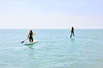 Paddle boarders. young man and woman on stand up paddleboard at sea. Water sport activity, SUP surfing. recreation sport paddling concept. sportive people in wetsuit