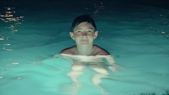 Smiling teenage boy in swimming pool at night. Concept of trip to warm countries and summer vacation