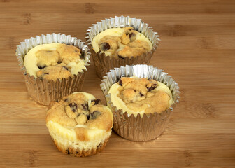 Cupcakes made by combining chocolate chip cookies and cheesecake in silver foil cupcake holders on a brown wood board.