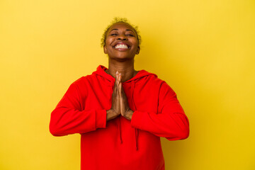 Young african american woman isolated on yellow background holding hands in pray near mouth, feels confident.