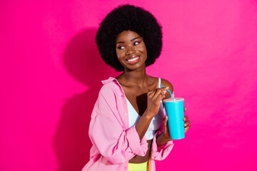 Photo of charming pretty dark skin lady wear casual shirt drinking soda looking empty space smiling isolated pink color background