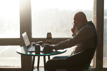 photographer is editing his photo while sitting at a table near the window.