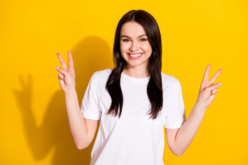 Photo of pretty shiny young lady dressed white t-shirt showing two v-signs smiling isolated yellow color background