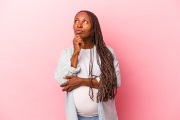 Young african american pregnant woman isolated on pink background looking sideways with doubtful...