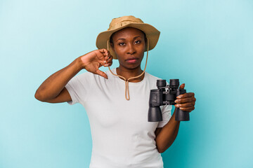 Young african american woman holding binoculars isolated on blue background showing a dislike gesture, thumbs down. Disagreement concept.