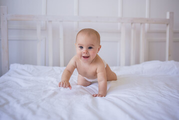 a happy baby girl in a diaper crawls on a white cotton blanket on the bed in the room