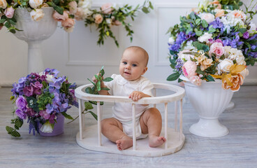 a baby girl in a white bodysuit with lace sits in chair on a background with flowers