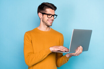 Photo of funny brunet millennial working guy type laptop wear spectacles brown sweater isolated on blue color background