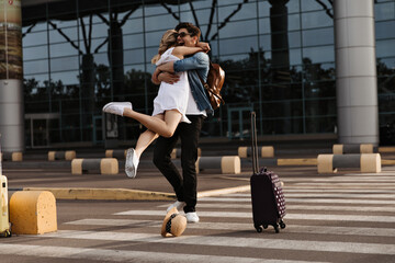 Happy brunette man hugs his girlfriend in white dress. Woman meets boyfriend in airport. Tourist...