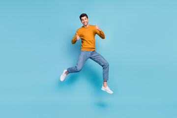 Photo of funky cute young man wear yellow sweater smiling jumping high showing thumbs up isolated...