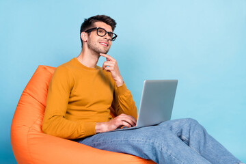 Portrait of attractive dreamy cheery guy sitting in chair using laptop typing isolated over bright blue teal color background