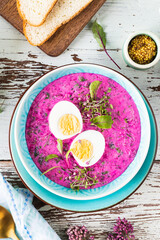 Cold soup made from beets, cucumbers and garnished with an egg in a blue plate on a wooden background. Top view.