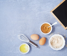 Ingredients for homemade oat pancake with whole grain oat, coconut sugar, vanilla syrup, organic eggs next to black chalkboard on light blue background. Healthy food recipe. Top view. Copy Space.