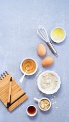 Ingredients for homemade oat pancake with whole grain oat, coconut sugar, vanilla syrup, organic eggs next to a notebook in a pen, light background. Healthy food recipe. Top view. Copy Space.