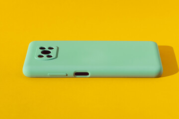 Light green silicone case for a smartphone on a yellow background, copy space.