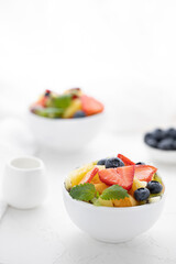 Fresh fruit salad with fresh strawberries, kiwi, apricots and blueberries, decorated with leaves of fresh mint in white plates on a white table