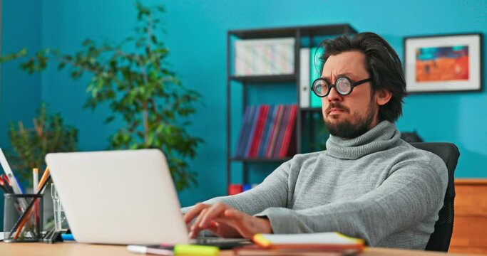 Weird man works in front of computer, writes back emails to customers, taps on laptop keyboard, makes puzzled faces, ponders, happy at work, cabaret performer, meme, nerd with funny glasses