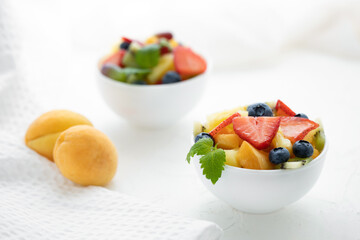 Fresh fruit salad with fresh strawberries, kiwi, apricots and blueberries, decorated with leaves of fresh mint in white plates on a white table