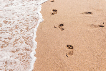 Human footprints on the sand with sea water. Foam from a wave on the sand with traces. A foamy ocean wave on a seashell beach