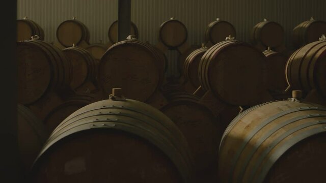 Aged wooden barrels with a wine , brandy or whiskey in a big warehouse . Dolly , gimbal movement a long row of wine barrels at a vintage winery with alcohol . Wine preparation and fermenting process
