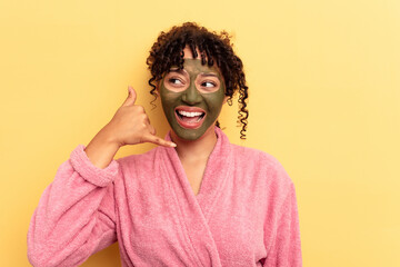 Young mixed race wearing facial mask isolated on yellow background showing a mobile phone call gesture with fingers.