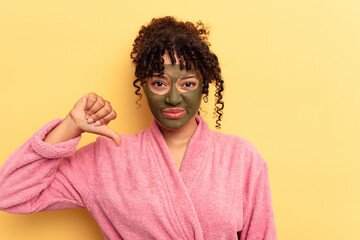 Young mixed race wearing facial mask isolated on yellow background showing a dislike gesture, thumbs down. Disagreement concept.