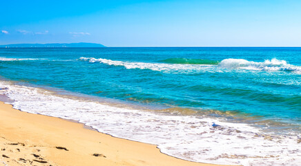 Blue sea with a foamy wave and a sandy beach. Summer panorama of nature