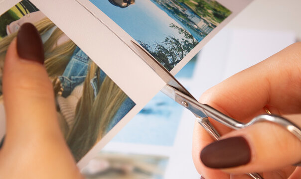 A woman cuts out photos with people in close-up. A girl uses scissors to cut printed polaroid photos for an album. A person holds a polaroid photo in his hands against the background of other photos.