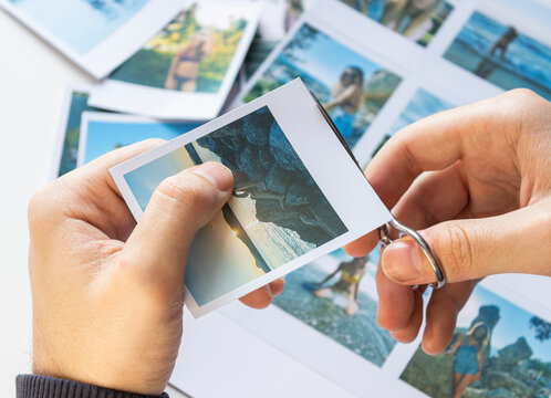 A man cuts out photos with people in close-up. A man uses scissors to cut printed polaroid photos for an album. A person holds a polaroid photo in his hands against the background of other photos.