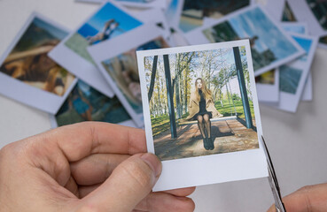 A person holds a polaroid photo in his hands against the background of other photos. Photo in hand close-up. A person looks at a photo from a polaroid.