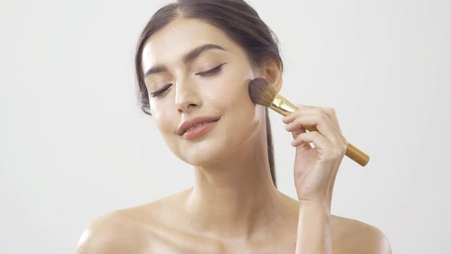 Beautiful woman applying poder at white background. She using makeup brush to apply poder her face.