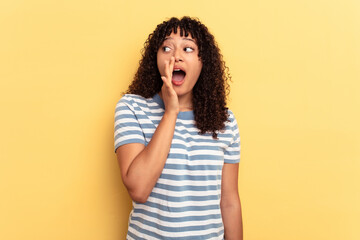 Young mixed race woman isolated on yellow background is saying a secret hot braking news and looking aside