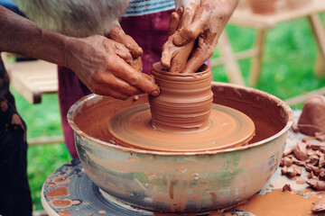 Family working on pottery wheel. Master teaching kid to creating on the pottery wheel. Craftsman's hands and child